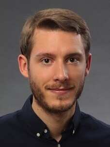 Herr Budich mit kurzem Haar und Bart, vor neutralem grauen Hintergrund.